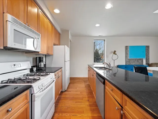 a kitchen with granite countertop a refrigerator a sink a stove and white cabinets