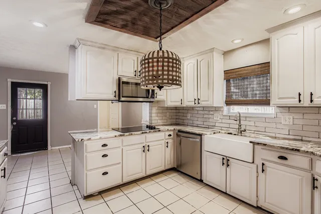 a kitchen with white cabinets a sink appliances and a window