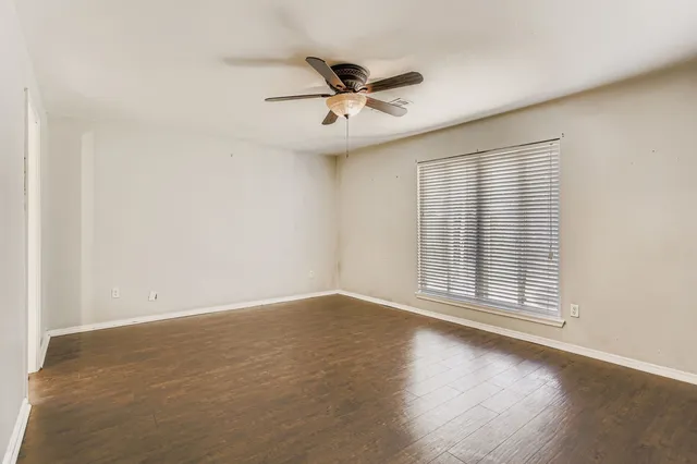 an empty room with wooden floor fan and windows