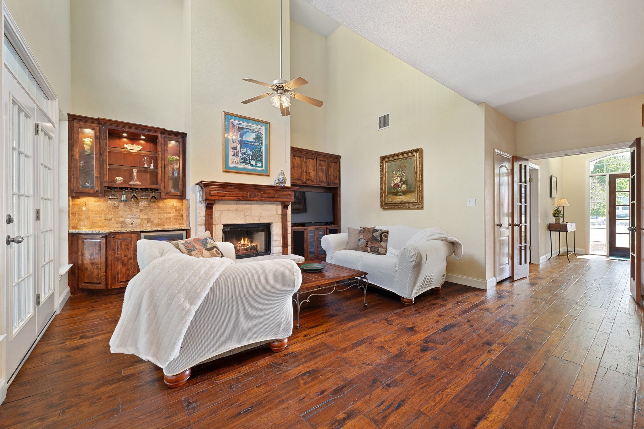 19045 Venture Drive Lago Vista, TX 78645 - Photo 8 of 40 Living room with a towering ceiling, a stone fireplace, dark wood-style floors, ceiling fan, and french doors