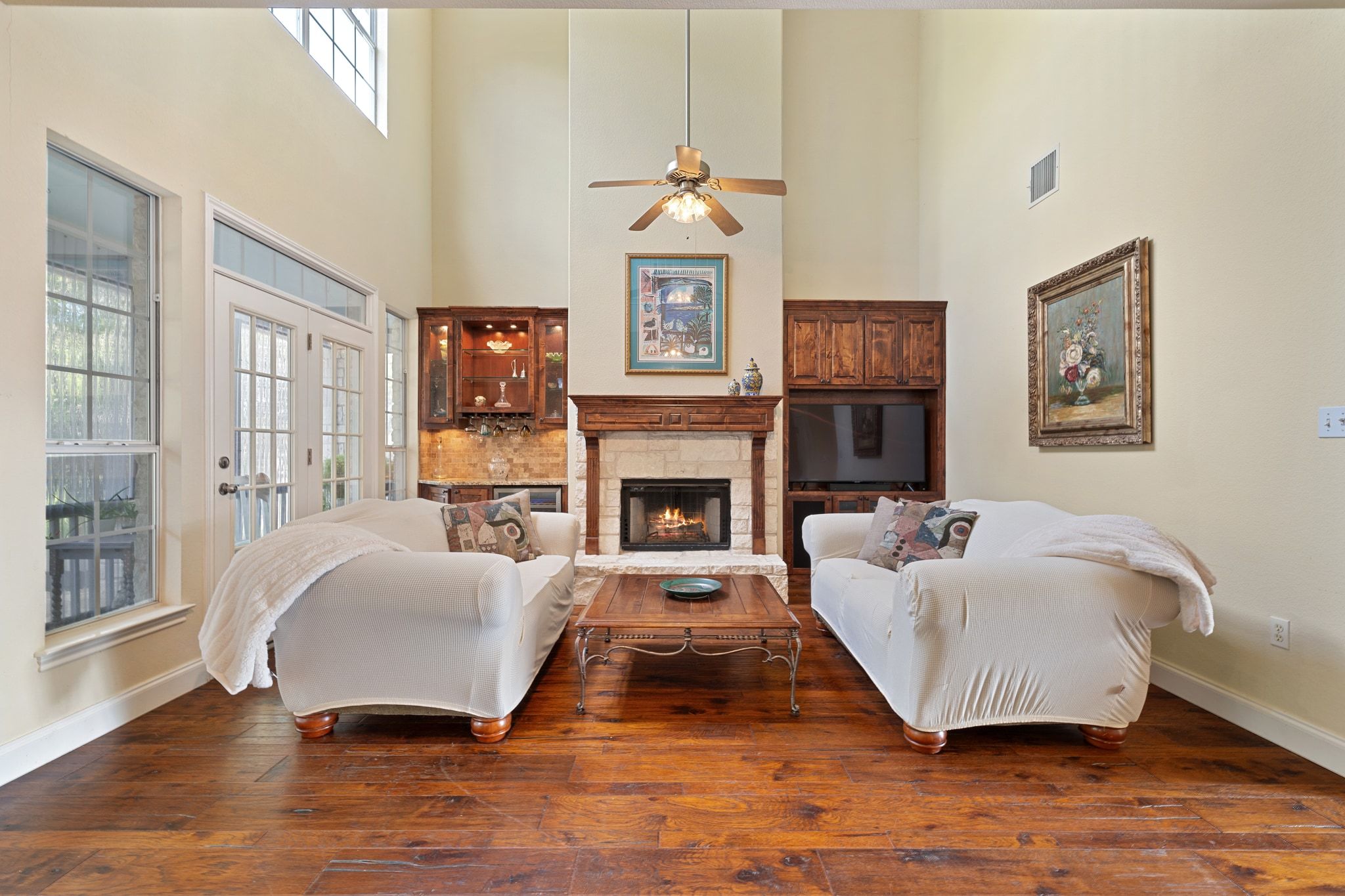 19045 Venture Drive Lago Vista, TX 78645 - Photo 9 of 40 Living room featuring a stone fireplace, healthy amount of natural light, ceiling fan, hardwood / wood-style floors, and a towering ceiling