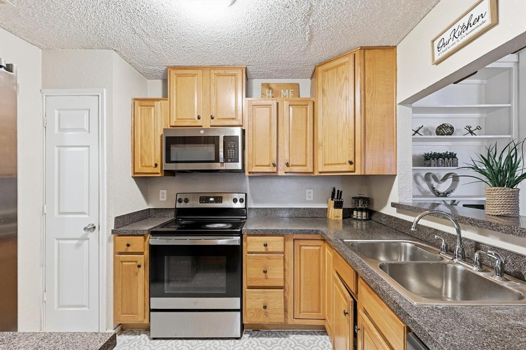 1312 Hackamore Street Mesquite, TX 75149 - Photo 7 of 23 Kitchen featuring stainless steel appliances, dark countertops, a textured ceiling, light wood finish cabinets, and open shelves