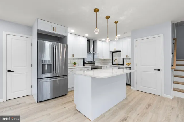 a large kitchen with stainless steel appliances kitchen island granite countertop a stove a sink a refrigerator and white cabinets with wooden floor