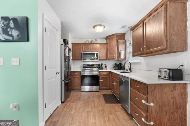 a kitchen with stainless steel appliances granite countertop a refrigerator a sink dishwasher a stove and white countertops with wooden floor