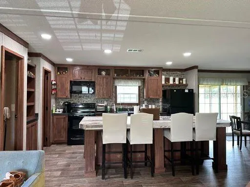 a kitchen with stainless steel appliances kitchen island granite countertop a dining table chairs and a refrigerator