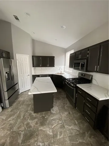 a large kitchen with stainless steel appliances a stove a sink dishwasher a refrigerator and white cabinets with wooden floor