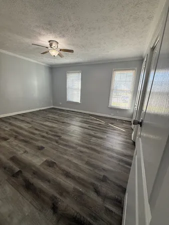 a view of an empty room with wooden floor and fan