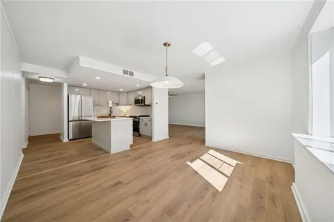 a view of empty room with wooden floor and kitchen