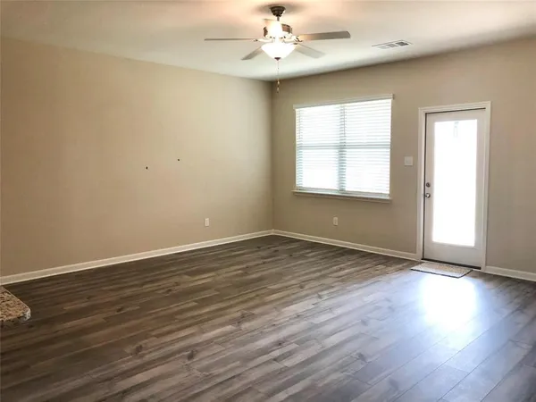 an empty room with wooden floor chandelier fan and windows