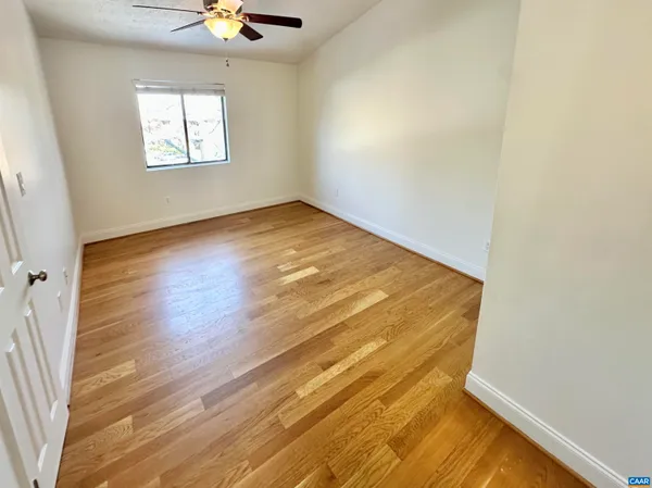 an empty room with wooden floor fan and windows