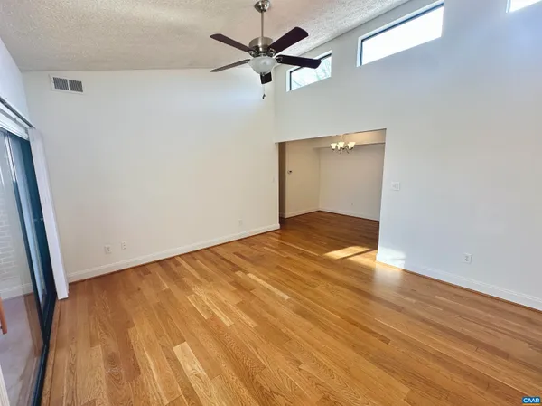 an empty room with wooden floor ceiling fan and window