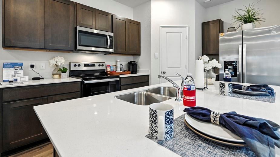 646 Glee Stem Road Lavon, TX 75166 - Photo 7 of 17 Modern kitchen featuring ample white countertop space, dark wood-finish cabinetry, stainless steel appliances, and an undermount double basin sink