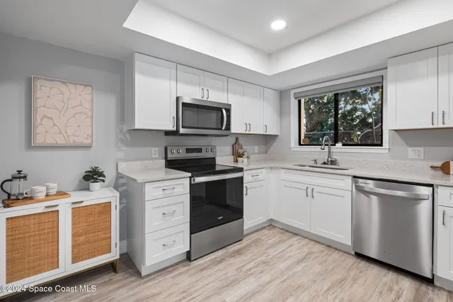 a kitchen with white cabinets appliances a sink and a window