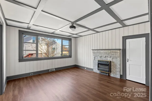 an empty room with wooden floor fireplace and windows