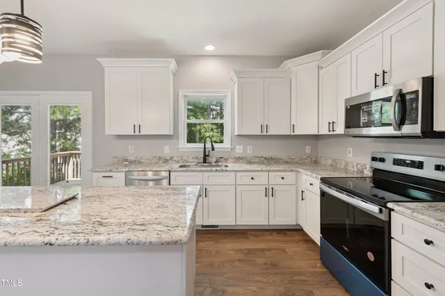 a kitchen with kitchen island granite countertop a stove a sink and white cabinets with wooden floor