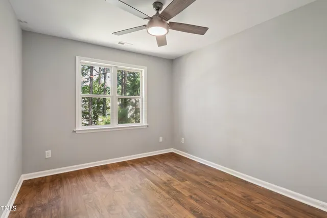 an empty room with wooden floor window and ceiling fan