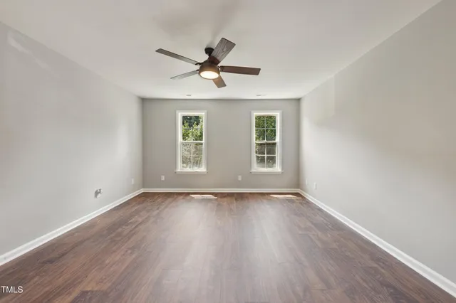 an empty room with wooden floor ceiling fan and windows