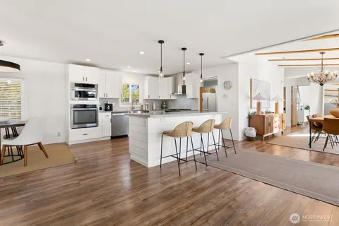 a kitchen with stainless steel appliances kitchen island granite countertop a stove top oven a sink a dining table and chairs with wooden floor