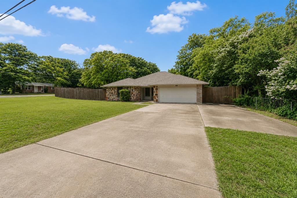 1001 Rosebud Drive Azle, TX 76020 - Photo 2 of 36 Stone facade residence with an attached two-car garage, featuring a concrete driveway, expansive front lawn, and mature trees