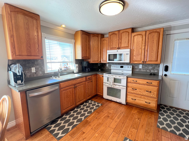 1852 East 3500th Street South Vernal, UT 84078 - Photo 14 of 46 Kitchen featuring dark countertops, white appliances, wood finish cabinetry, light wood-style floors, and ornamental molding
