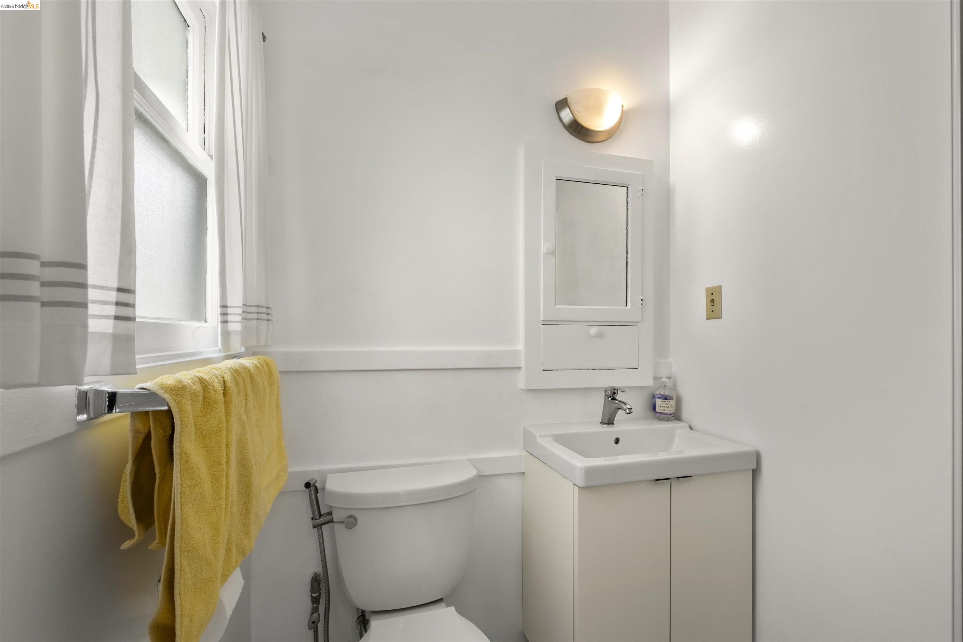 2444 Virginia Street, Unit B Berkeley, CA 94709 - Photo 35 of 39 Compact bathroom featuring a white wall-mounted sink with cabinet storage, a mirrored medicine cabinet, and a functional window with a towel bar