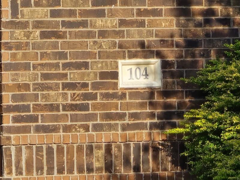 104 Anthony Lane Red Oak, TX 75154 - Photo 5 of 6 Brick facade with a light-colored address plaque featuring dark numerals, accented by vibrant green shrubbery