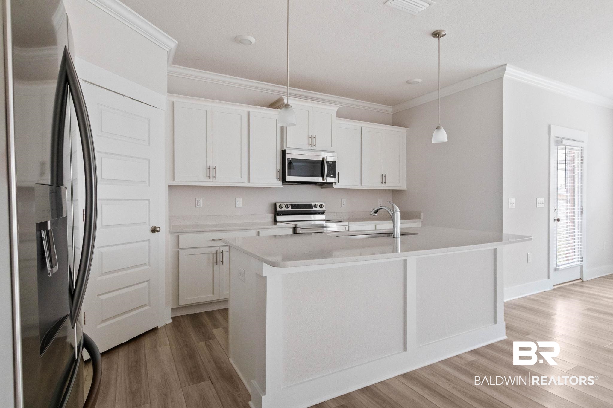 1710 Grouse Street Foley, AL 36535 - Photo 25 of 76 Kitchen featuring white cabinetry, light-toned countertops, a central island with an undermount sink, stainless steel appliances, and wood-finish flooring
