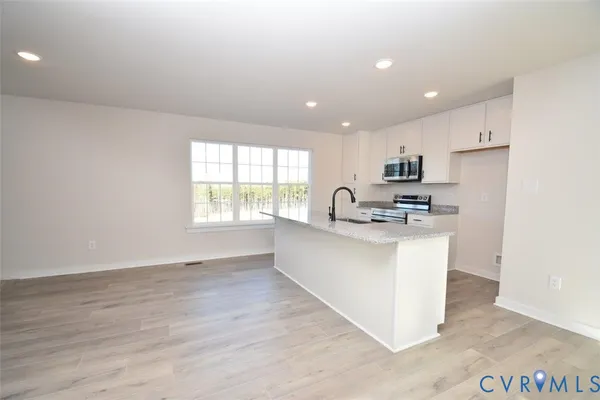 a kitchen with stainless steel appliances kitchen island granite countertop a stove a sink a refrigerator and white cabinets with wooden floor