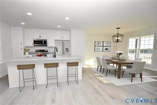 a kitchen with stainless steel appliances granite countertop a stove a refrigerator a microwave a dining table and chairs with wooden floor