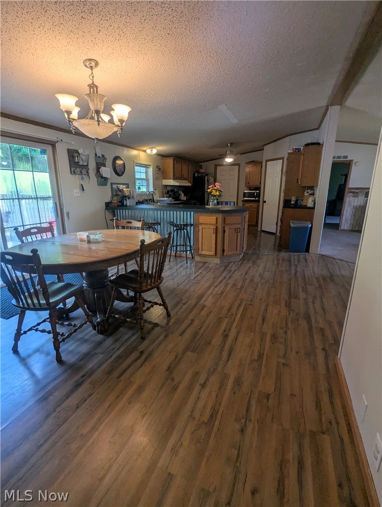 17960 Raven Road Salesville, OH 43778 - Photo 12 of 27 Open-concept living area featuring wood-finish flooring, a dining area with pendant lighting, and a kitchen with wood cabinetry and a corrugated metal accent island