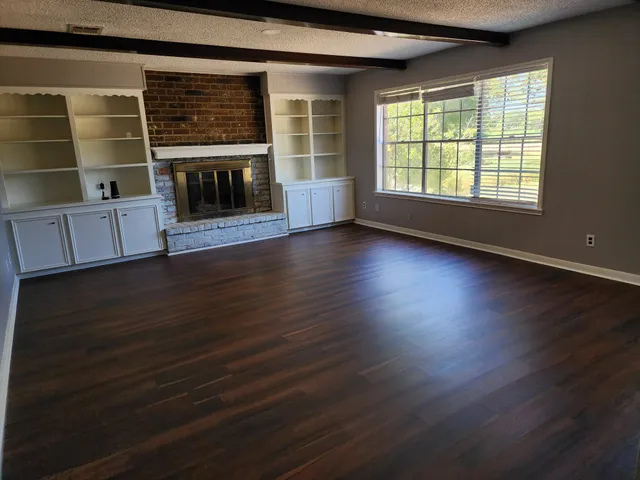 an empty room with wooden floor fireplace and windows