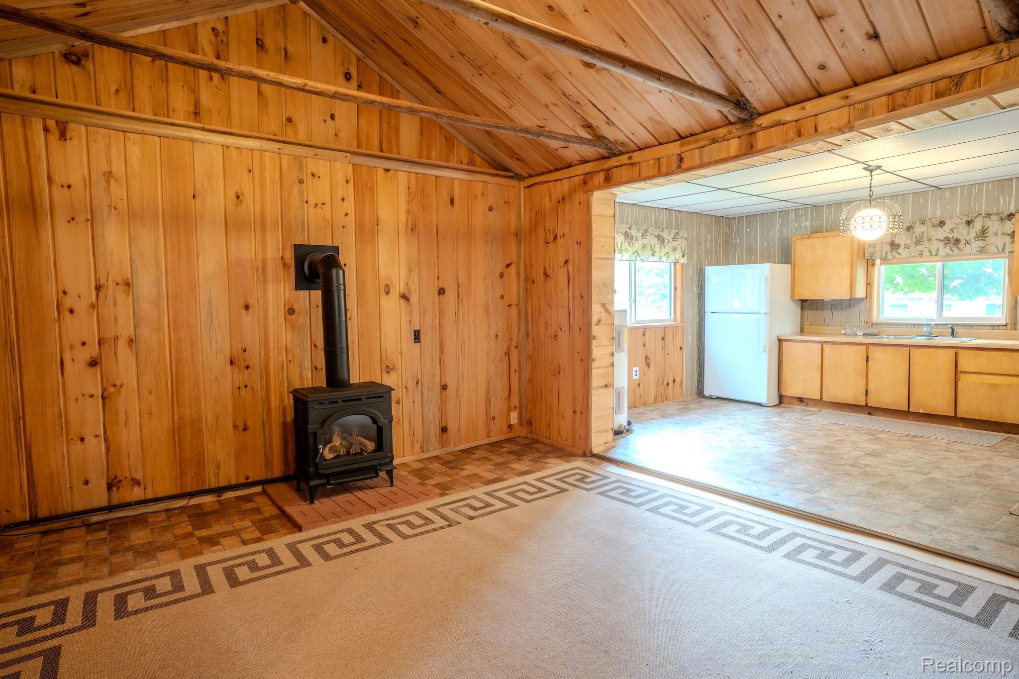 4350 Shrew Road Lincoln, MI 48742 - Photo 13 of 32 Vaulted wood-paneled ceiling, wood-paneled walls, and a black cast-iron stove with visible piping