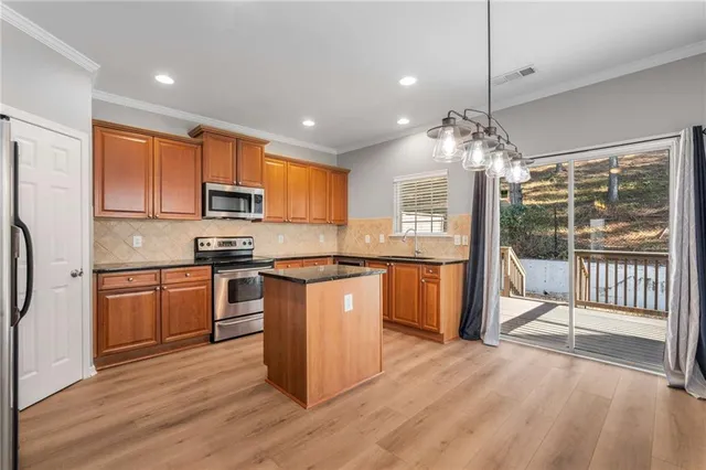 a kitchen with stainless steel appliances granite countertop a refrigerator a sink dishwasher a stove top oven and a dining table with wooden floor