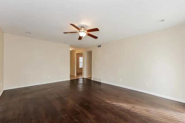 a view of an empty room with chandelier fan and wooden floor