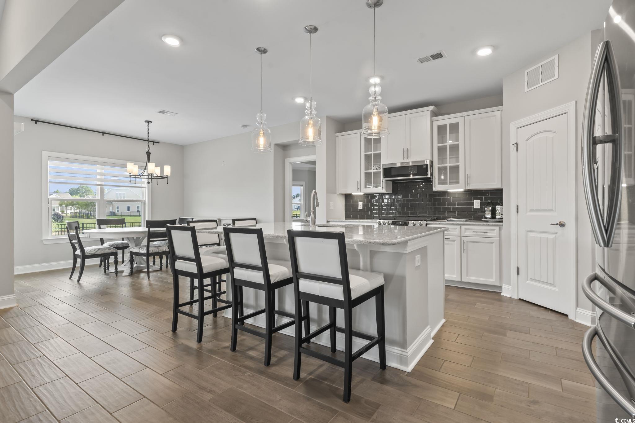 583 Hickman Street Surfside Beach, SC 29575 - Photo 20 of 40 Kitchen featuring glass insert cabinets, backsplash, white cabinetry, a kitchen breakfast bar, and decorative light fixtures