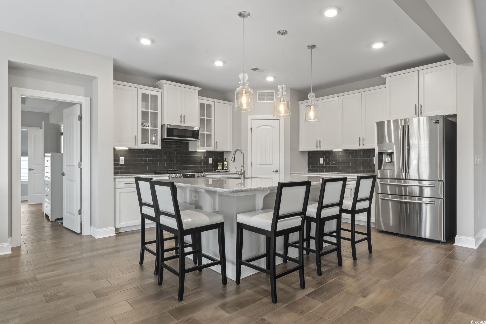 583 Hickman Street Surfside Beach, SC 29575 - Photo 21 of 40 Kitchen featuring a breakfast bar area, stainless steel appliances, glass insert cabinets, decorative light fixtures, and white cabinetry