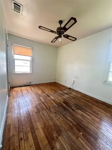 an empty room with wooden floor fan and windows
