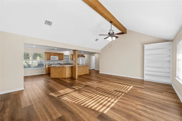 a view of a living room with kitchen island wooden floor and a ceiling fan