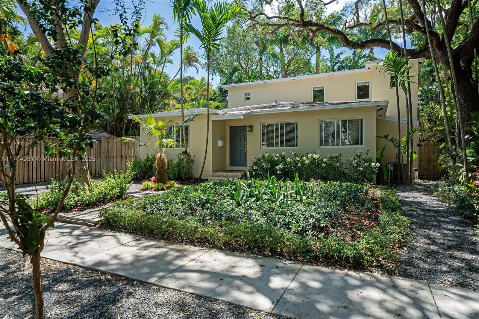 a view of a white house next to a yard with plants and trees