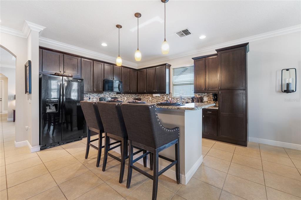 4436 Azure Isle Way Kissimmee, FL 34744 - Photo 20 of 35 a kitchen with stainless steel appliances kitchen island granite countertop a refrigerator a stove a oven a sink with a dining table and chairs