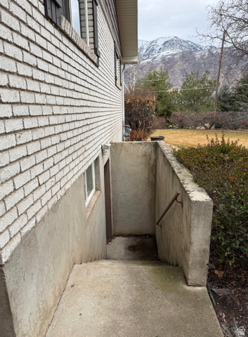 1360 Carterville Road Orem, UT 84097 - Photo 37 of 41 White brick exterior with a concrete foundation, a concrete stairwell with a metal handrail, and a snowy mountain backdrop