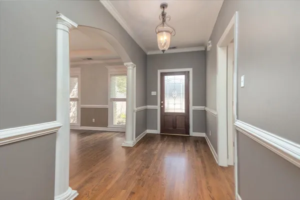 an empty room with wooden floor chandelier and windows