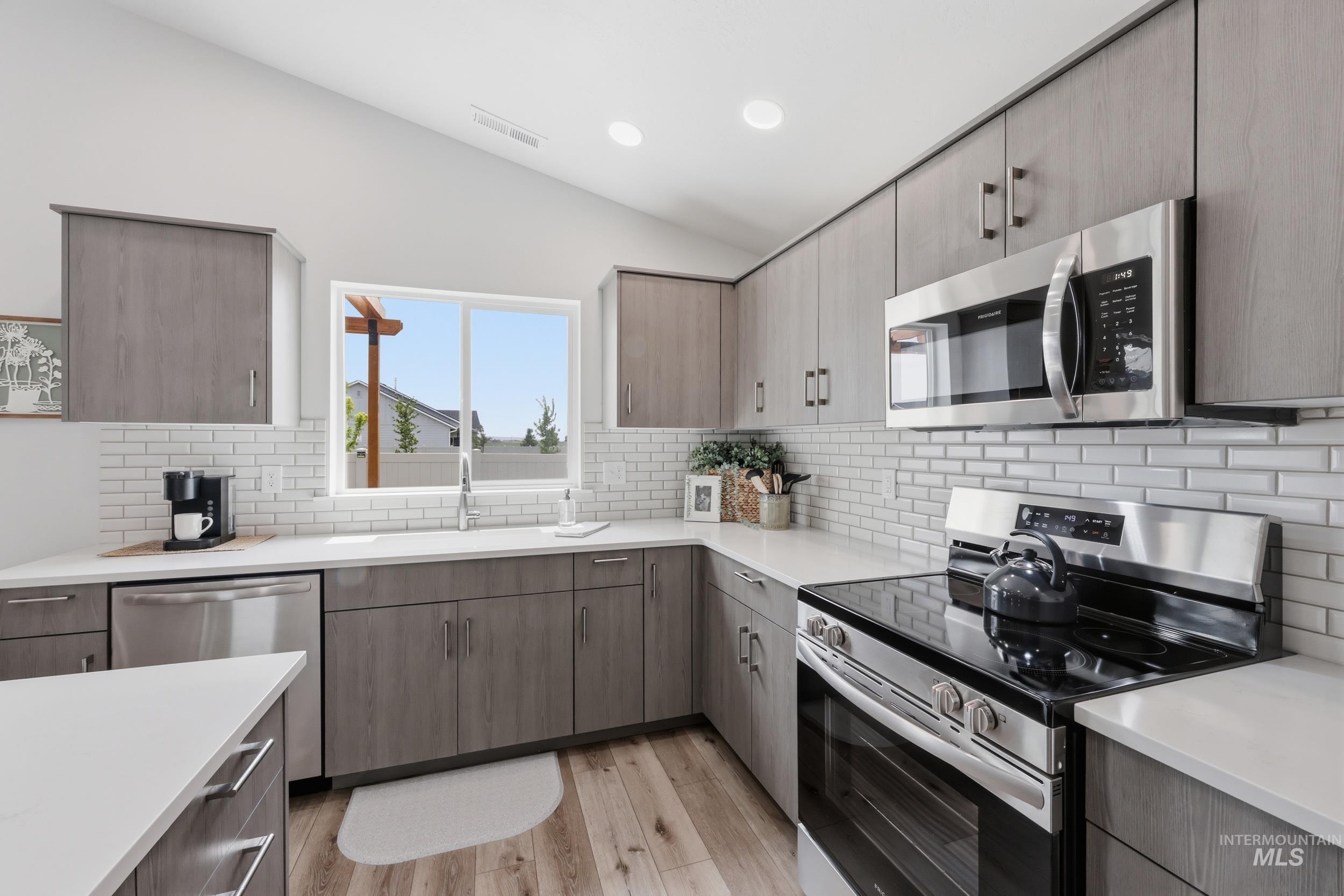 3665 W Lane Meridian, ID 83642 - Photo 8 of 42 Modern kitchen featuring a central island with countertop seating, stainless steel appliances, wood-finish flooring, white subway tile backsplash, and ample cabinetry