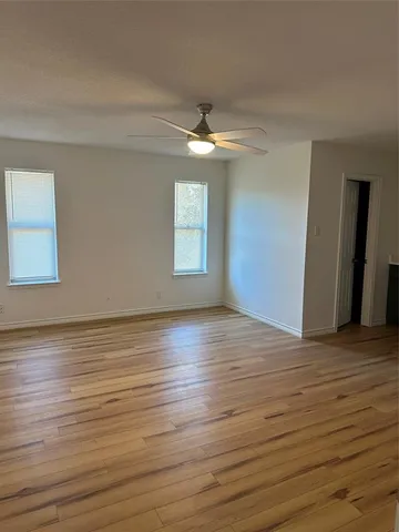 an empty room with wooden floor chandelier fan and windows