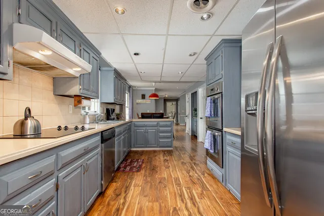 a kitchen with stainless steel appliances a refrigerator a sink dishwasher a stove and white cabinets with wooden floor