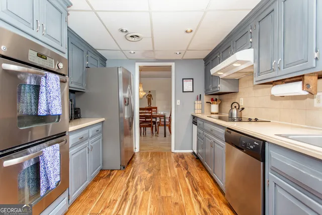 a kitchen with stainless steel appliances granite countertop a refrigerator a sink dishwasher a stove and white countertops with wooden floor