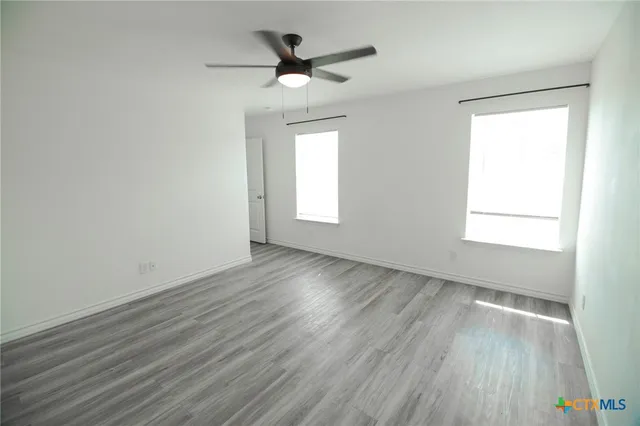 an empty room with wooden floor chandelier fan and windows
