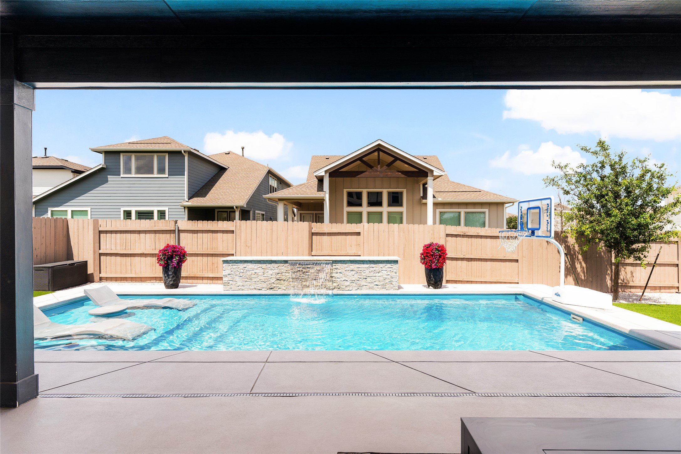 7917 Edmondson Bend Austin, TX 78744 - Photo 20 of 24 Outdoor swimming pool with built-in lounge areas, a stone-clad waterfall feature, and a concrete patio surround