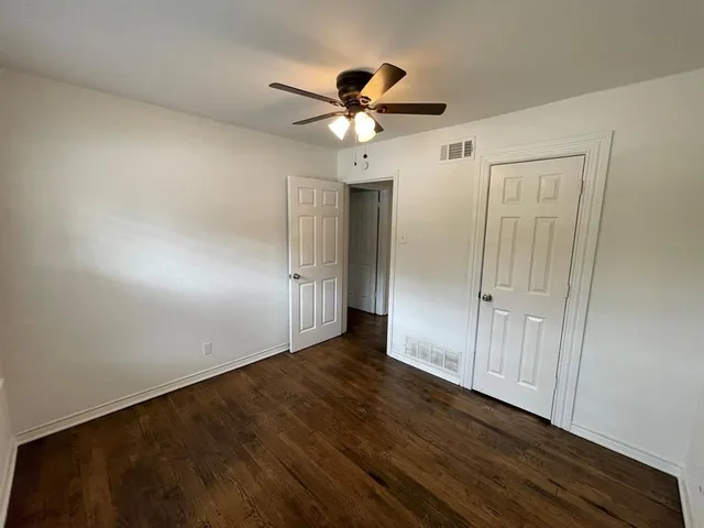 an empty room with wooden floor fan and windows