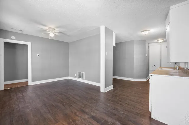 a view of an empty room with wooden floor and a kitchen